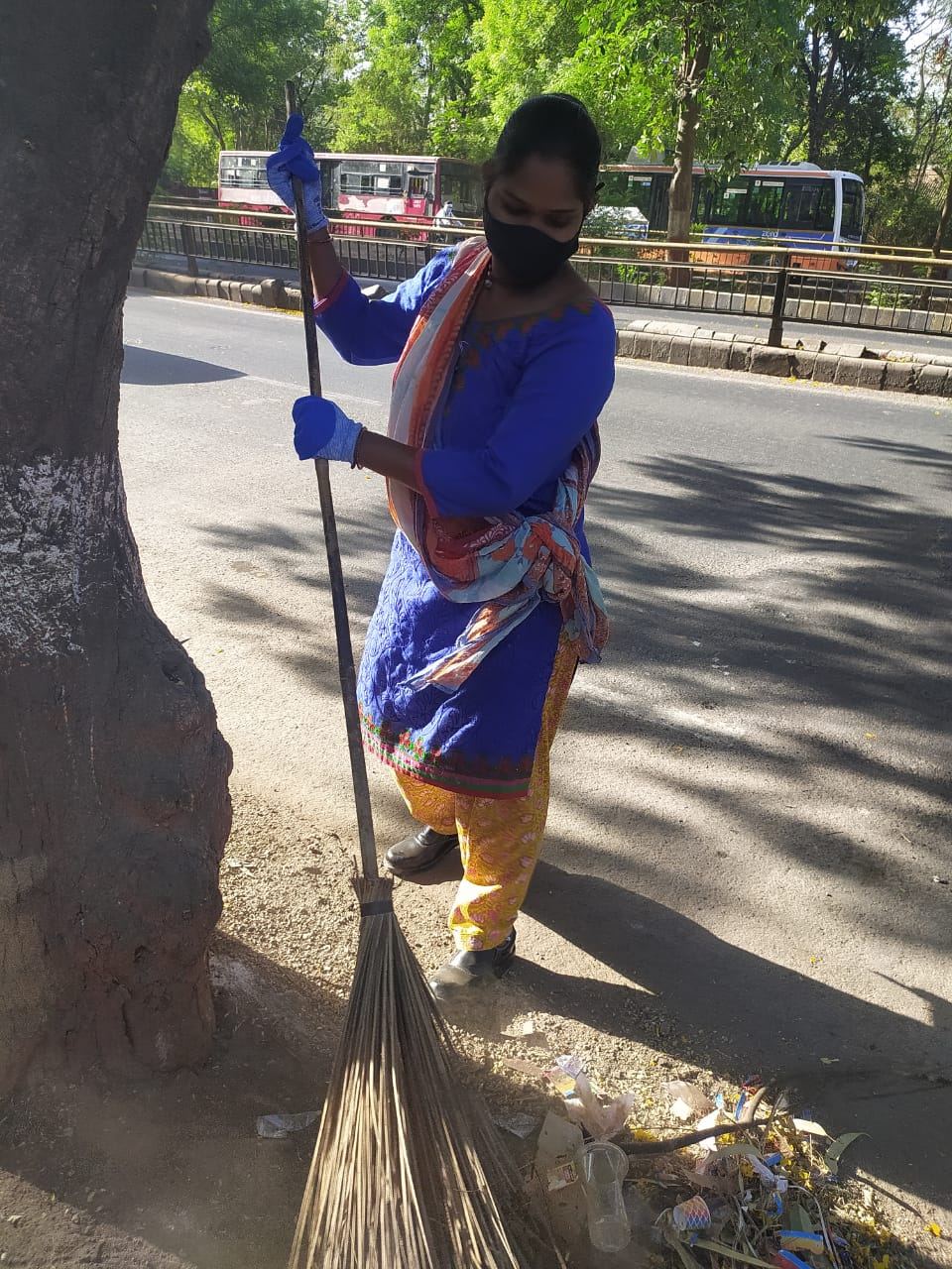 A woman sweeping the road wearing a mask and gloves